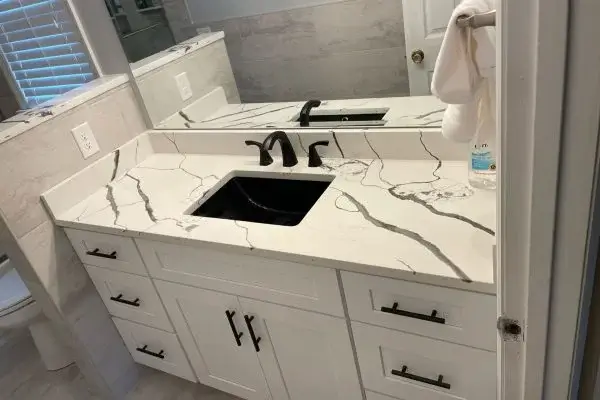 Modern bathroom vanity with white marble countertop and black fixtures, including an undermount sink and faucet